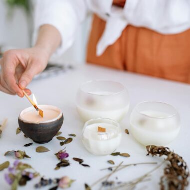 A hand lights a decorative candle among flowers and herbs, creating a serene ambiance.