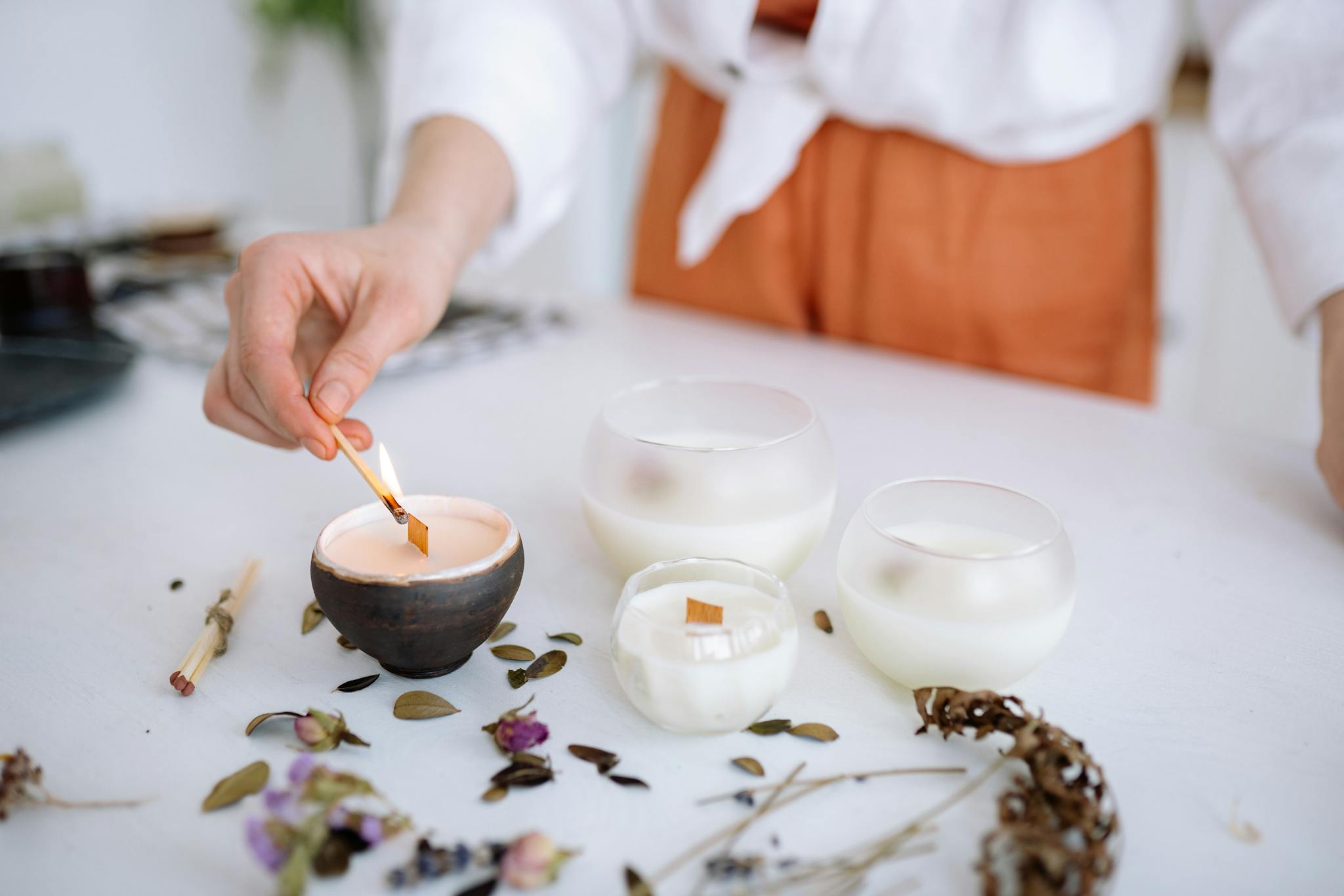 A hand lights a decorative candle among flowers and herbs, creating a serene ambiance.