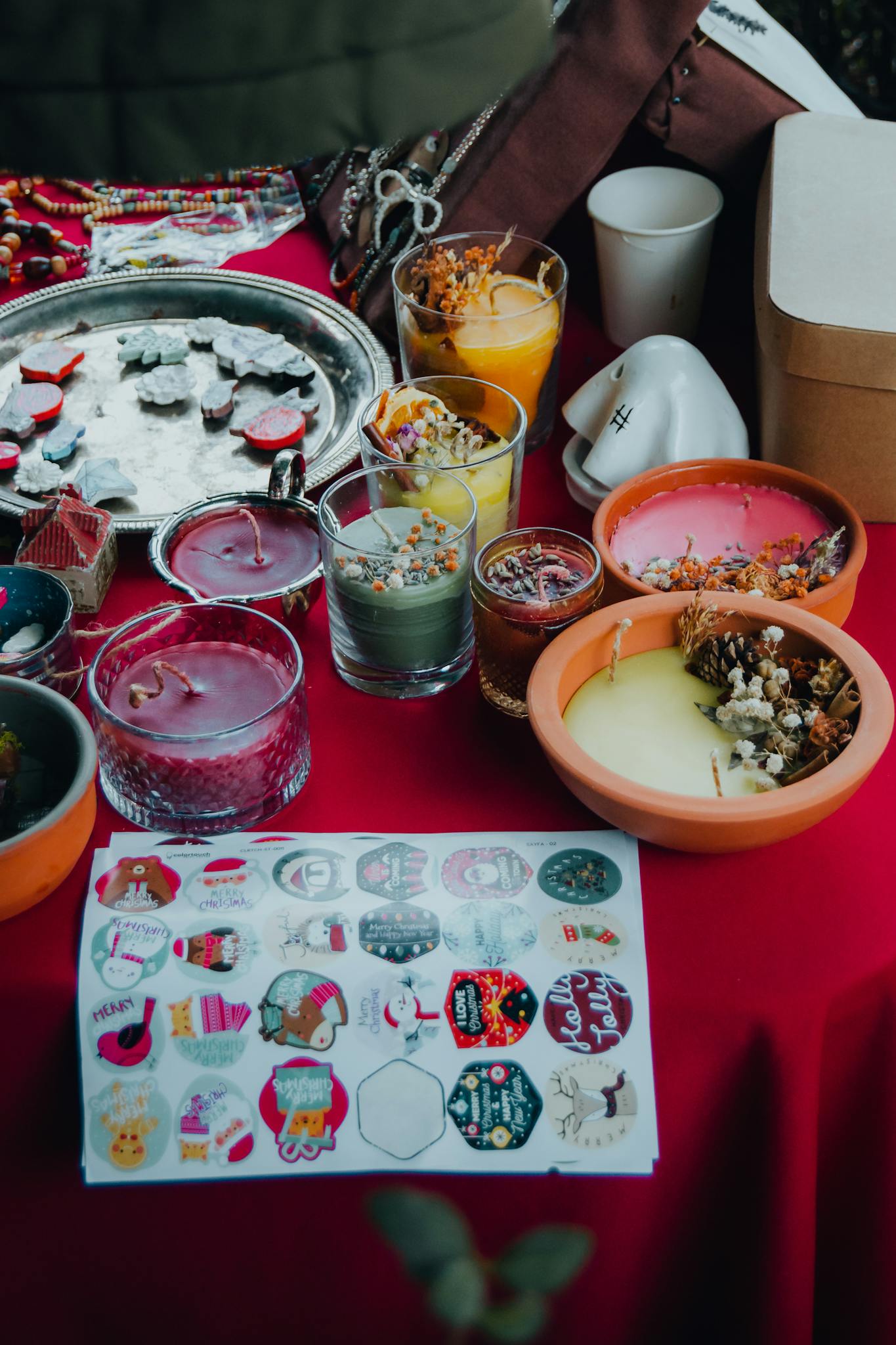 Vibrant collection of handmade candles and decorative stickers on a red tablecloth.