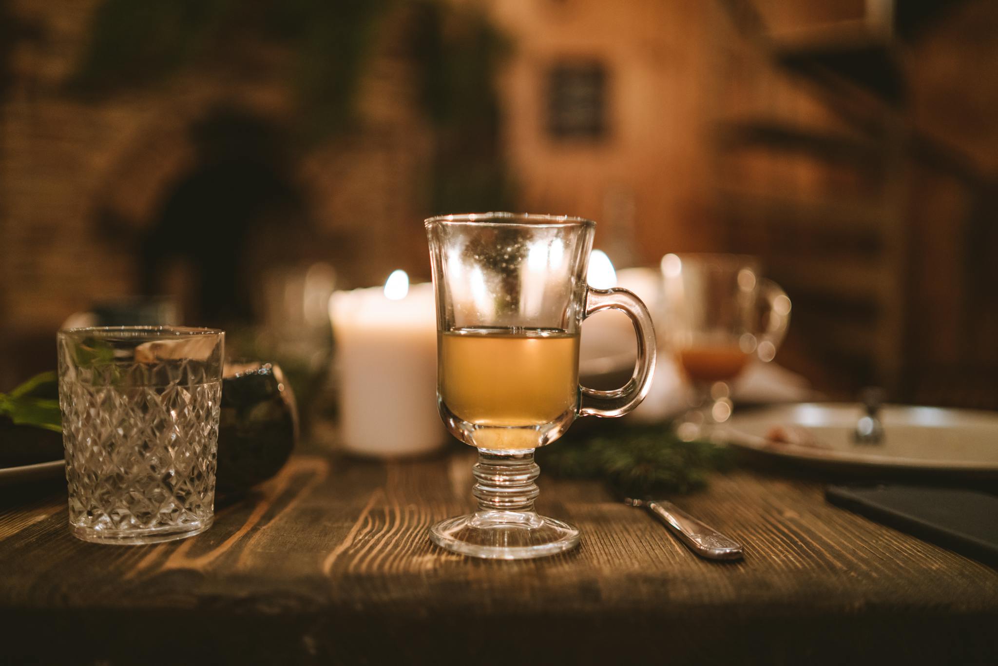 Warm holiday drink in glass cup on wooden table with candles and rustic decor, perfect for festive gatherings.